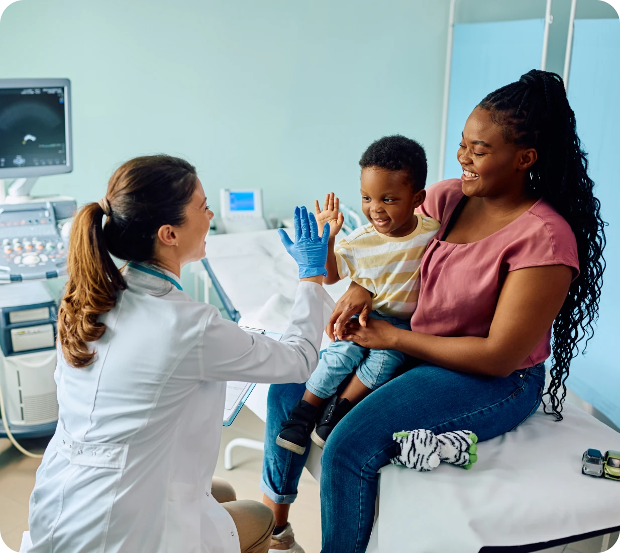 Doctor high-fiving child with mother nearby.