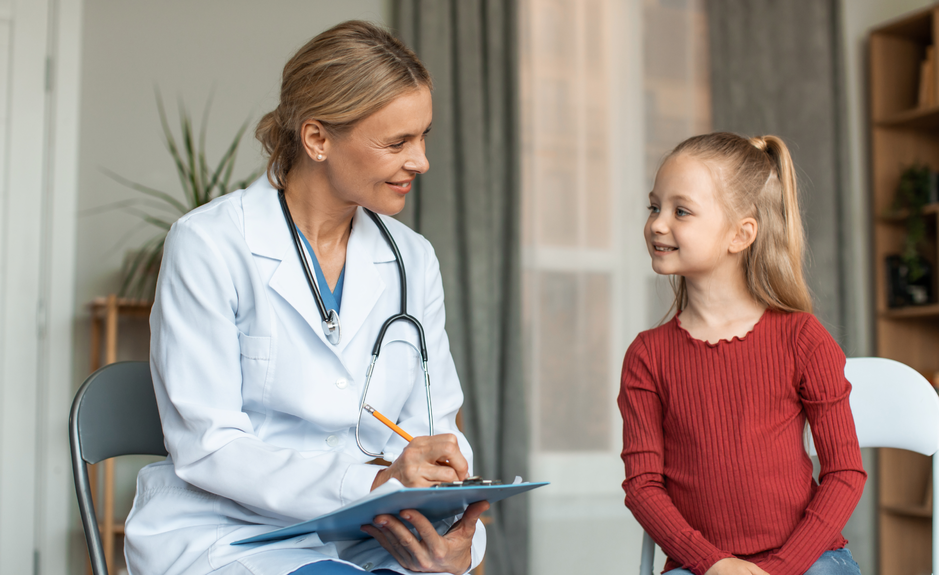 A doctor smiling and talking with a young girl in a medical office.